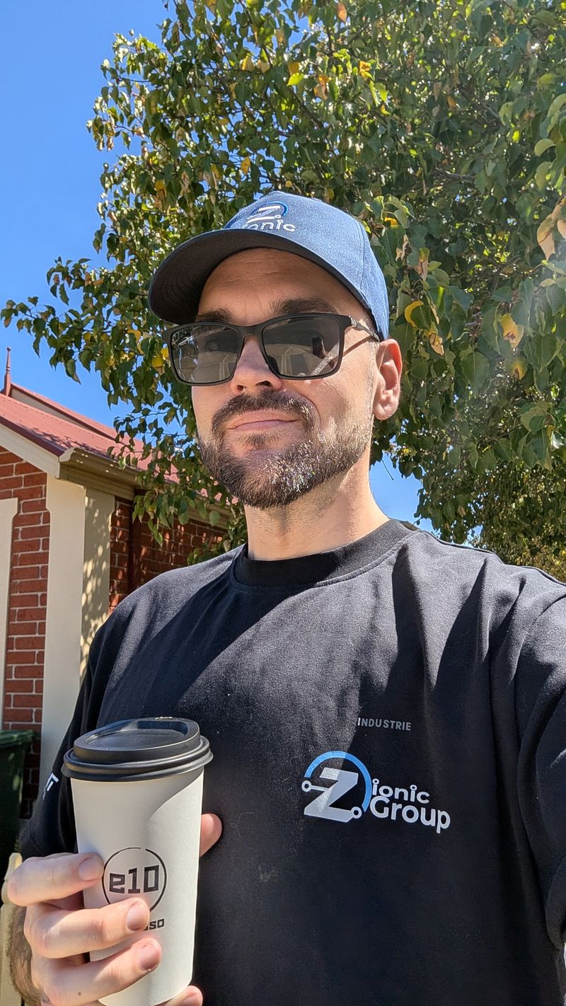 Daniel Bryant holding a coffee, wearing a Zionic Group cap and shirt